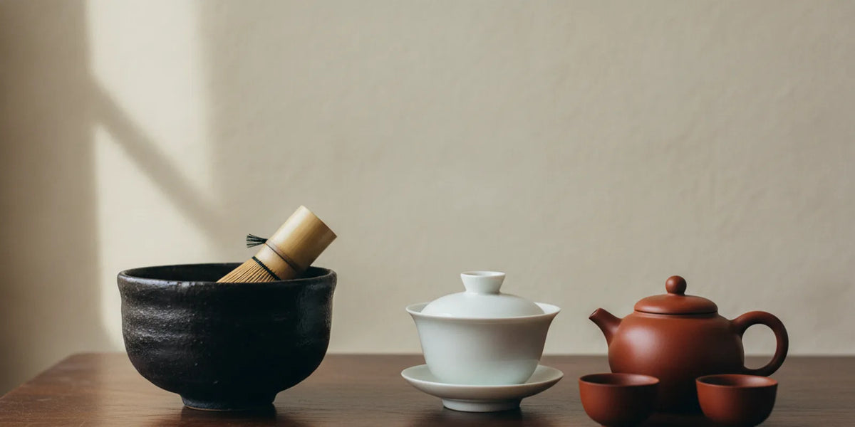 A Japanese tea bowl and whisk beside a Chinese gaiwan and small teapot on a tea table