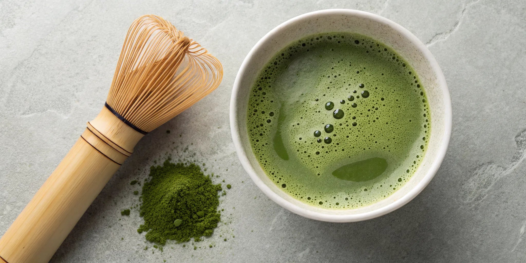 A bowl of frothy matcha with a bamboo whisk and matcha powder.