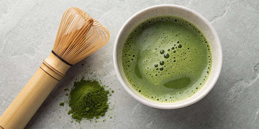 A bowl of frothy matcha with a bamboo whisk and matcha powder.