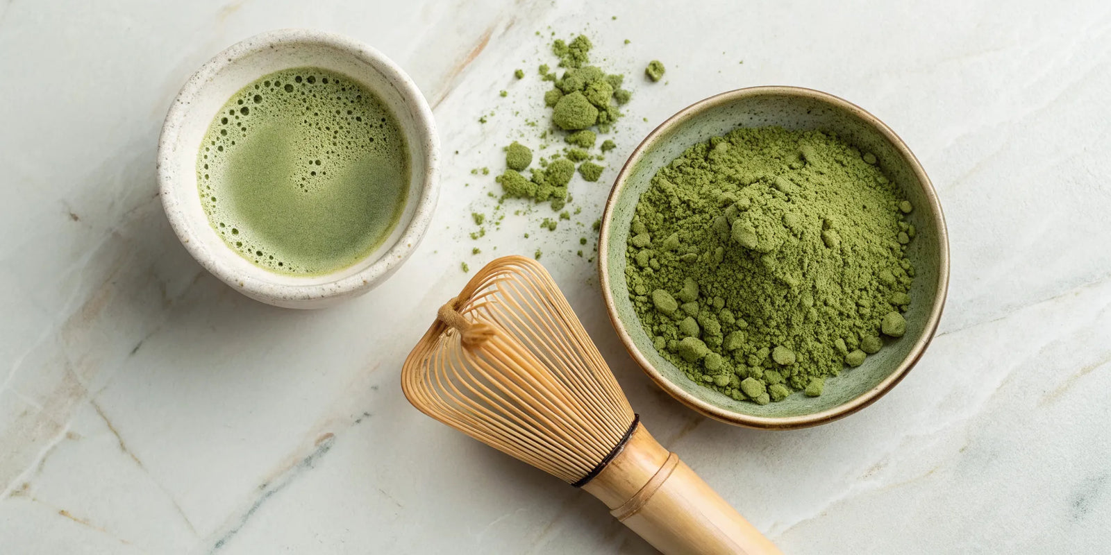 Matcha powder in a bowl with a bamboo whisk next to a prepared cup of matcha tea.