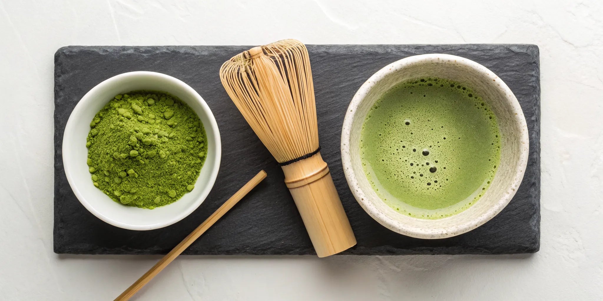 A traditional matcha tea set with a bamboo whisk, powder, and a freshly prepared bowl.