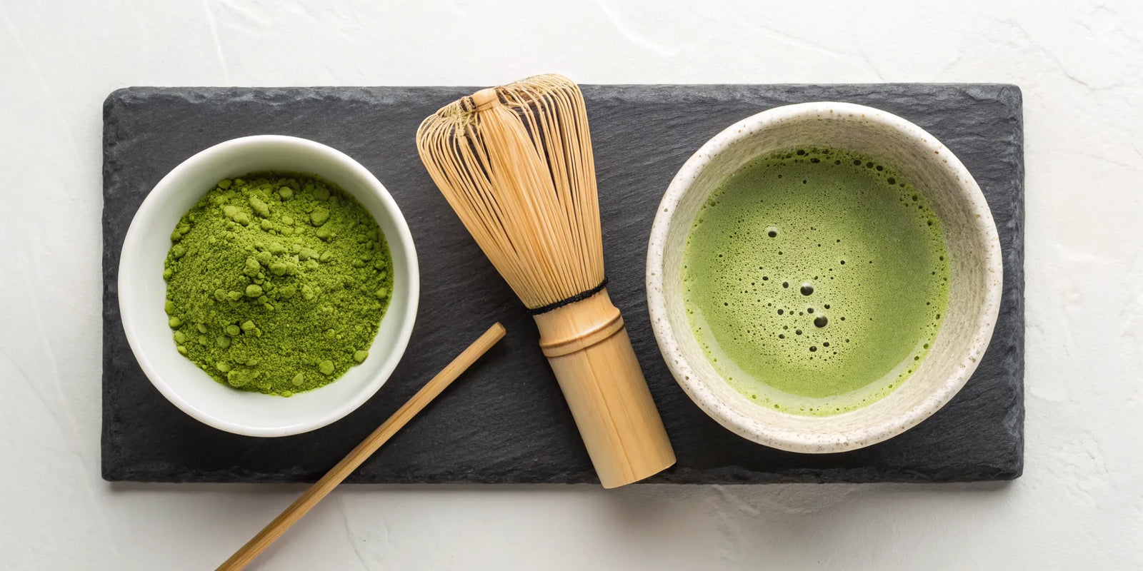 A traditional matcha tea set with a bamboo whisk, powder, and a freshly prepared bowl.