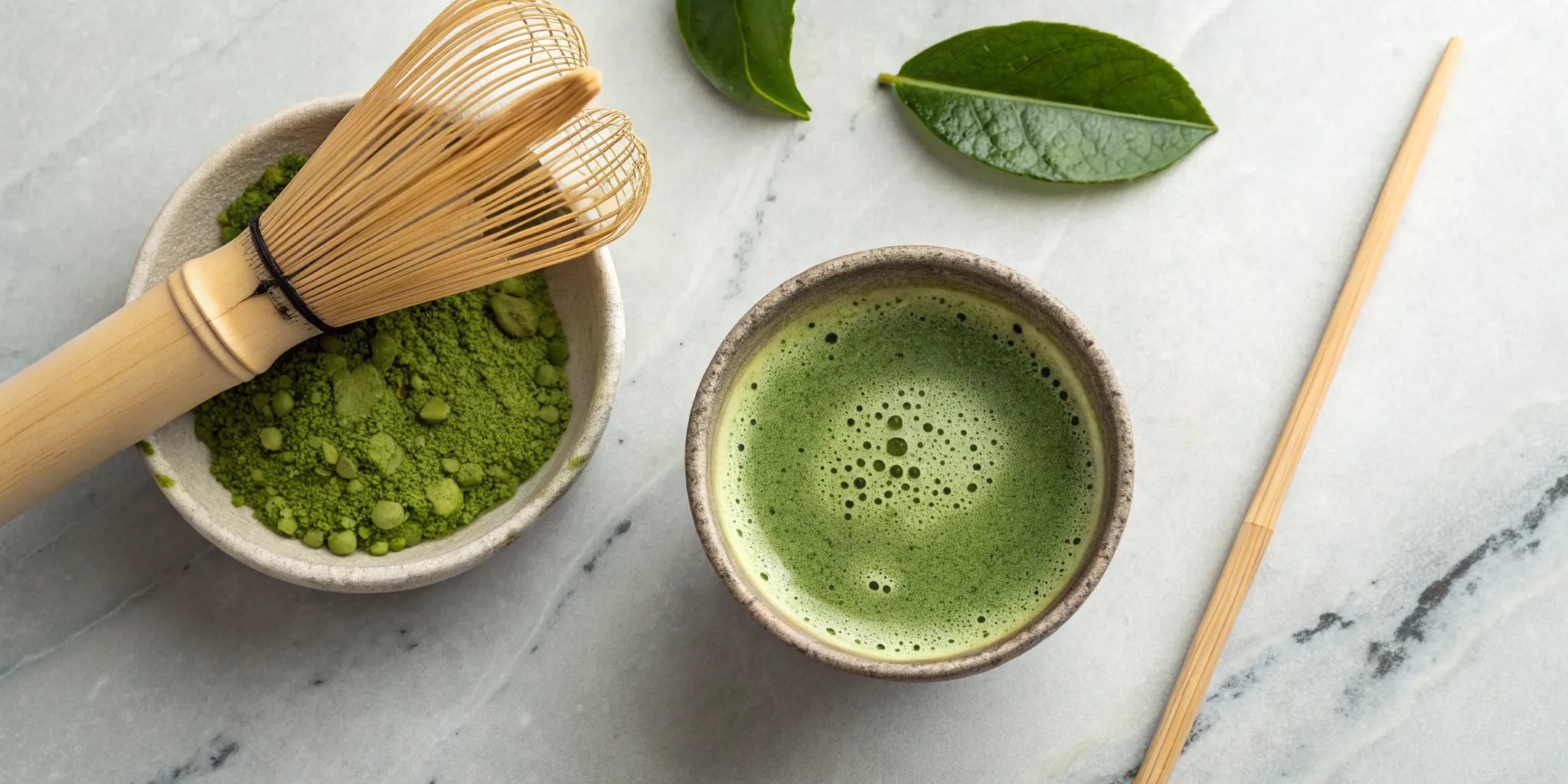 A bowl of prepared matcha tea next to a bamboo whisk and matcha powder.